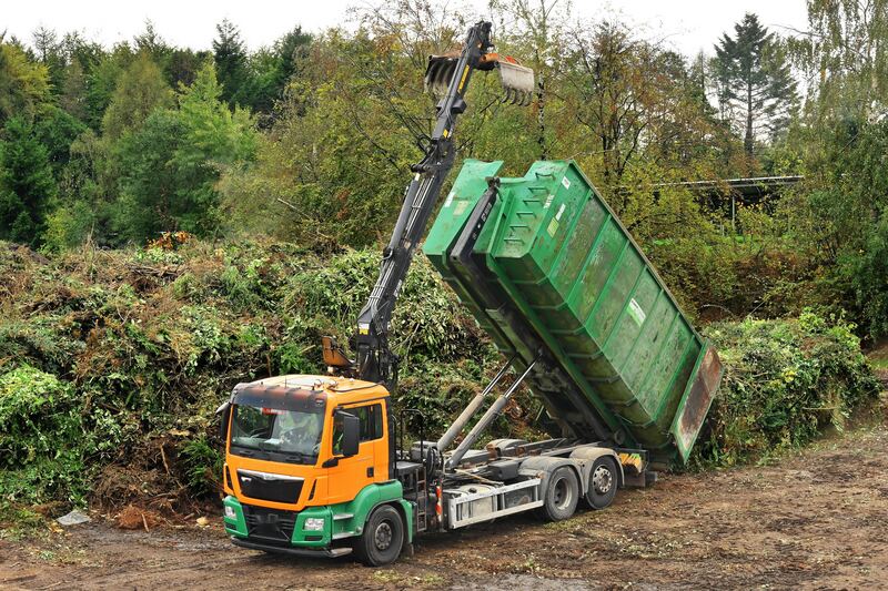 Benne verte relevée devant un grand tas de branches et de déchets verts